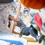 Side view of Caucasian female climber in early 20s gripping hand and foot holds while working out on bouldering wall in modern sport climbing center.